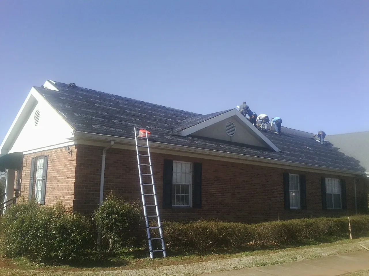 Crew tearing shingles off a brick ranch roof with a ladder set — Emergency Roof Repair work by our crew in Fillmore