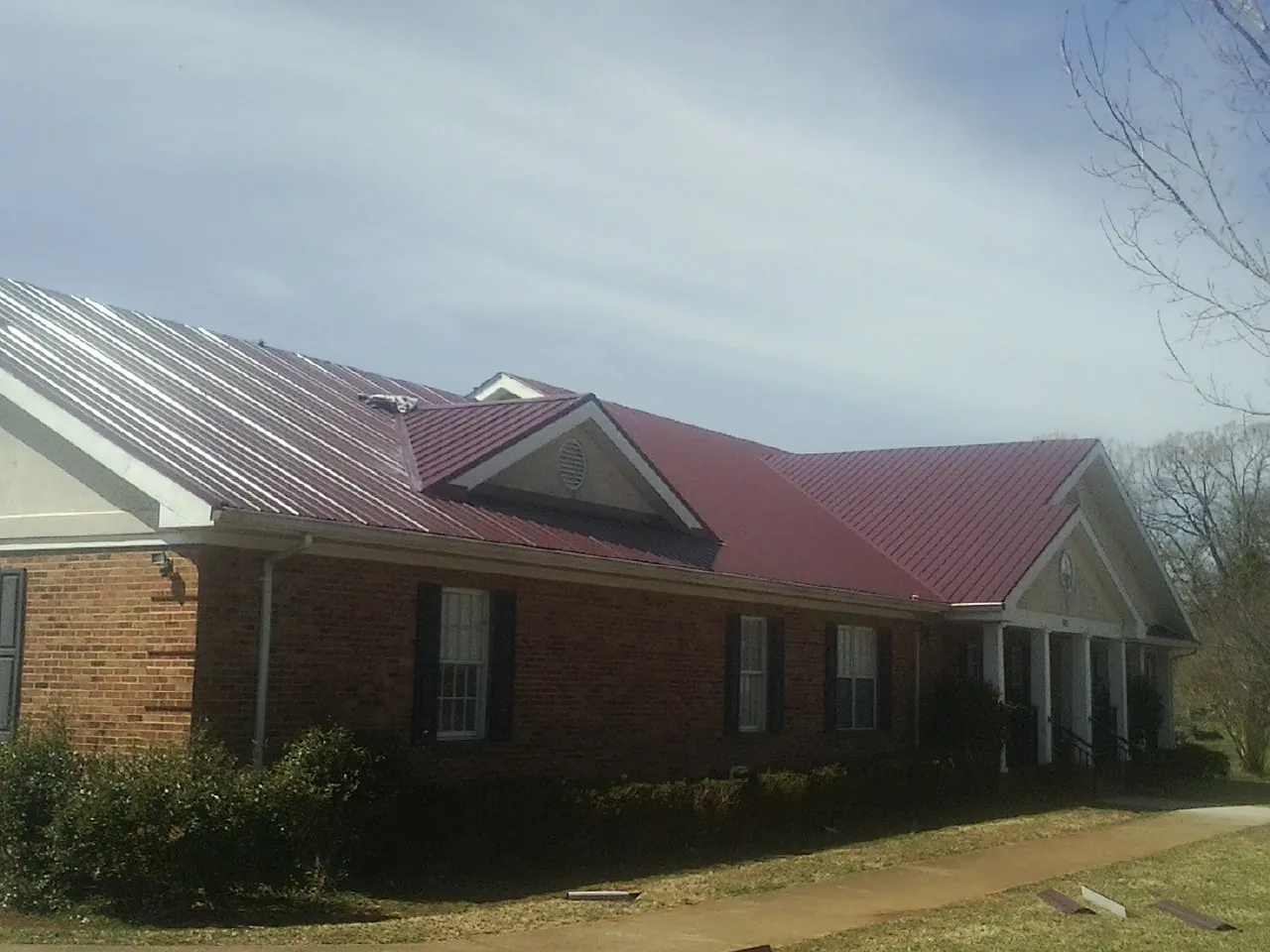 Red metal roof with gabled entries on a long brick building, from a Hail Damage Roof Repair job in Fillmore